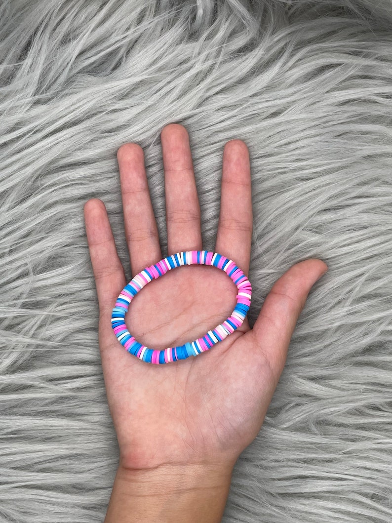 May include: A colorful beaded bracelet with pink, blue, and white beads. The bracelet is made of small, round beads that are strung together on a stretchy cord.