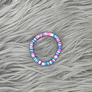 May include: A colorful bracelet made of small, round beads in shades of pink, blue, and white.