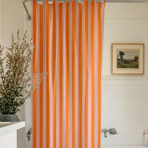 May include: Orange and pink striped shower curtain in a bathroom with a white bathtub and white tile walls.
