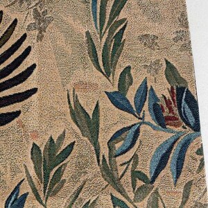 May include: Close-up of a woven textile with a botanical design. The fabric features a beige background with a pattern of dark green and blue leaves and floral elements. The design is detailed and intricate.