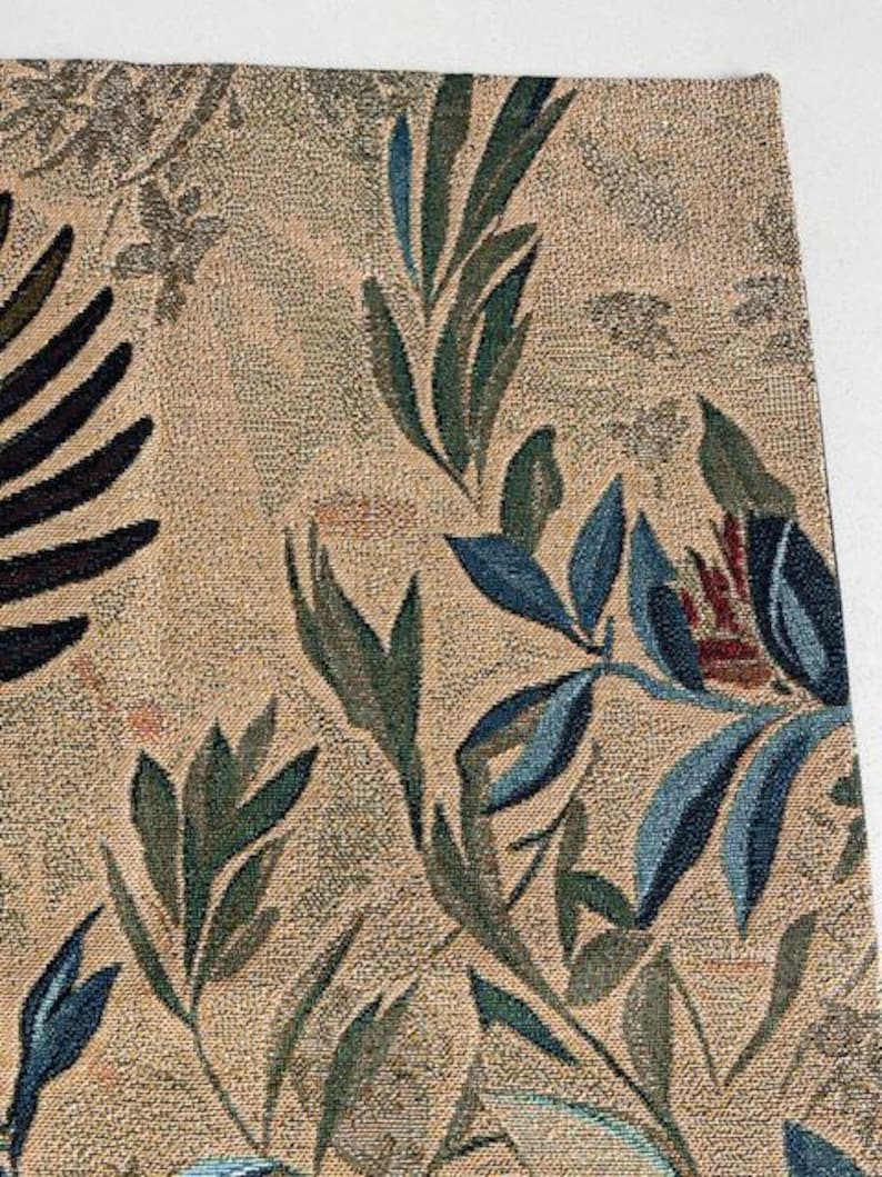 May include: Close-up of a woven textile with a botanical design. The fabric features a beige background with a pattern of dark green and blue leaves and floral elements. The design is detailed and intricate.