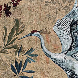 May include: Close-up of a tapestry featuring a crane with outstretched wings, set against a backdrop of floral and foliage patterns. The crane is primarily blue and white, with a red crown. The background is a beige color.