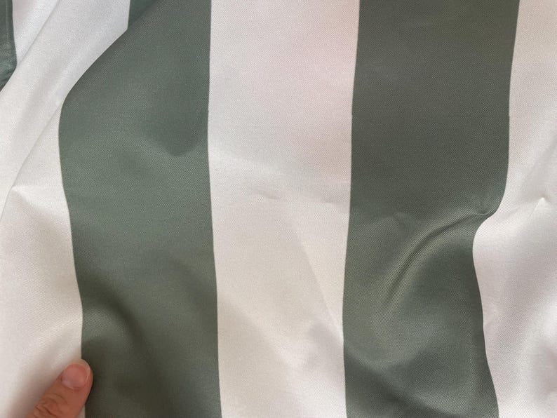 Peut inclure: Gros plan sur un tissu &agrave; rayures verticales. Des rayures larges altern&eacute;es, blanches et vert-gris, cr&eacute;ent un motif simple mais &eacute;l&eacute;gant. Le tissu semble lisse et l&eacute;g&egrave;rement r&eacute;fl&eacute;chissant.