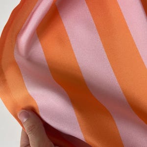 K&ouml;nnte beinhalten: Nahaufnahme eines rosa-orangen gestreiften Stoffes. Der Stoff hat eine glatte, seidige Textur.