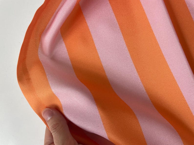 K&ouml;nnte beinhalten: Nahaufnahme eines rosa-orangen gestreiften Stoffes. Der Stoff hat eine glatte, seidige Textur.