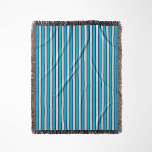 K&ouml;nnte beinhalten: Eine gewebte Wolldecke mit einem gestreiften Muster in Blau- und Beiget&ouml;nen. Die Decke hat einen Fransenrand.