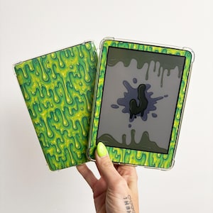 May include: A clear protective tablet case featuring a vibrant neon green and yellow slime drip pattern. The case is shown in two parts, with one piece displaying the slime design and the other framing a screen with a black slime splatter graphic.