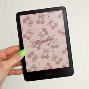 May include: A black Kindle e-reader with a pink and white cherry pattern background. The text "Kindle Girlie" is on the screen.