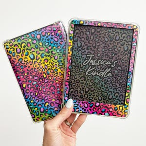 May include: Two clear Kindle cases with a colorful leopard print design. One case is closed, the other is open, displaying the screen with the text "Jessica's Kindle". The cases have a rainbow of colors.