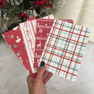 May include: A hand holds a fan of four Christmas-themed cards. The cards feature red and white patterns, including stripes, reindeer, snowflakes, and a plaid design. The cards are rectangular with rounded corners.