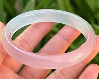 May include: A translucent jade bangle bracelet with a gradient of pale green to soft pink. The smooth, polished surface reflects light, showcasing the natural variations in color. This elegant piece of jewelry is a classic accessory.