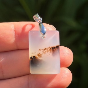 May include: A rectangular pendant made of translucent white stone featuring dark brown dendritic inclusions that resemble tree-like patterns. The stone is polished to a smooth finish and is attached to a silver-toned metal bail at the top.
