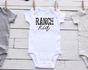 May include: White baby onesie with short sleeves and black text that reads "RANCH kid".