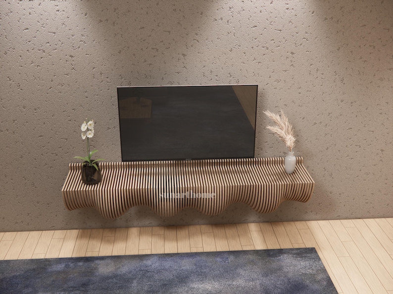 May include: A contemporary wooden floating shelf with a wavy design, supporting a flat-screen TV, a small plant, and a vase with decorative grass. The shelf is made of vertical wooden slats and is mounted on a textured grey wall.