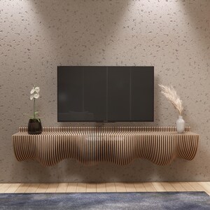 May include: A contemporary wooden TV unit with a wavy edge, mounted on a textured wall. A black television sits above the unit, with a vase of pampas grass and a potted plant. The room has a neutral colour scheme.
