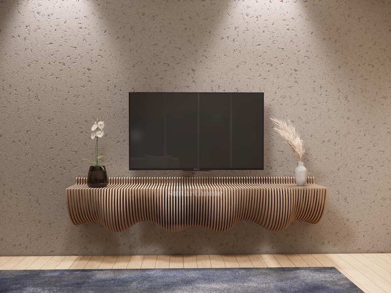 May include: A contemporary wooden TV unit with a wavy edge, mounted on a textured wall. A black television sits above the unit, with a vase of pampas grass and a potted plant. The room has a neutral colour scheme.