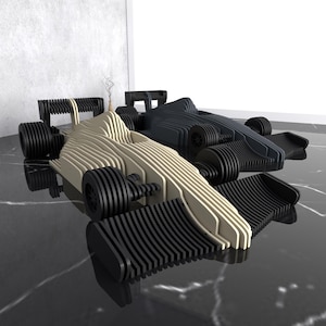 Puede incluir: Dos coches de carreras de Fórmula 1 de madera, uno beige y otro negro, se exhiben sobre una superficie reflectante. Los coches tienen diseños detallados de ruedas y carrocería, mostrando una estética moderna. El fondo es una pared gris neutra.