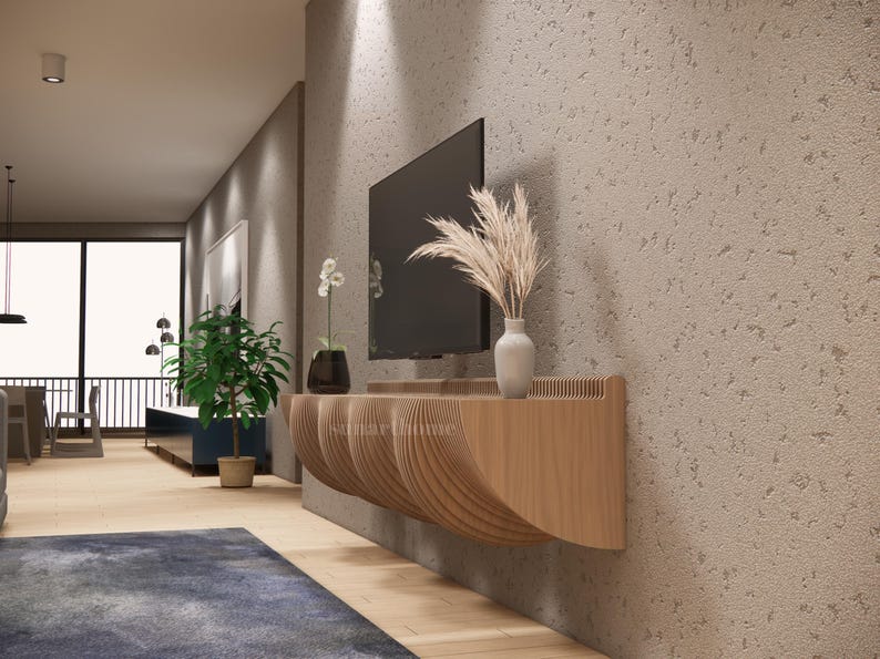 May include: A contemporary living room featuring a wall-mounted television above a wooden console with a distinctive, curved design. A vase with dried plants and a small white vase are on the console. A potted plant and a blue rug are also visible.
