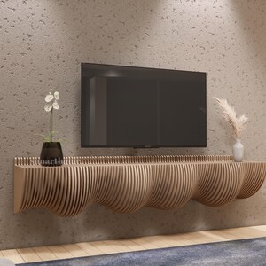 May include: A contemporary wooden TV unit with a distinctive, undulating design. The unit is crafted from light-toned wood and is fixed to a textured, light-brown wall. A black television is mounted above the unit. Decorative elements include a small plant and a vase.