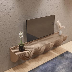 May include: A contemporary wooden TV shelf, featuring a unique wavy design. A flat-screen TV is mounted above the shelf. The shelf is adorned with a small white vase with dried flowers and a potted plant. The shelf is mounted on a textured wall.