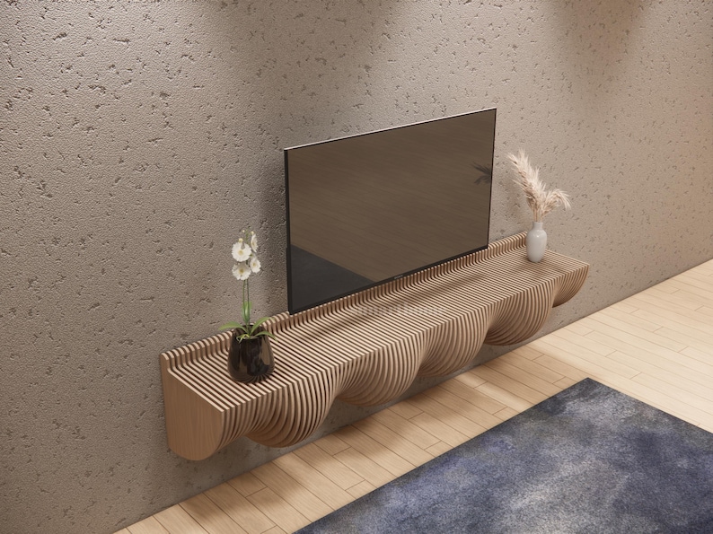 May include: A contemporary wooden TV shelf, featuring a unique wavy design. A flat-screen TV is mounted above the shelf. The shelf is adorned with a small white vase with dried flowers and a potted plant. The shelf is mounted on a textured wall.