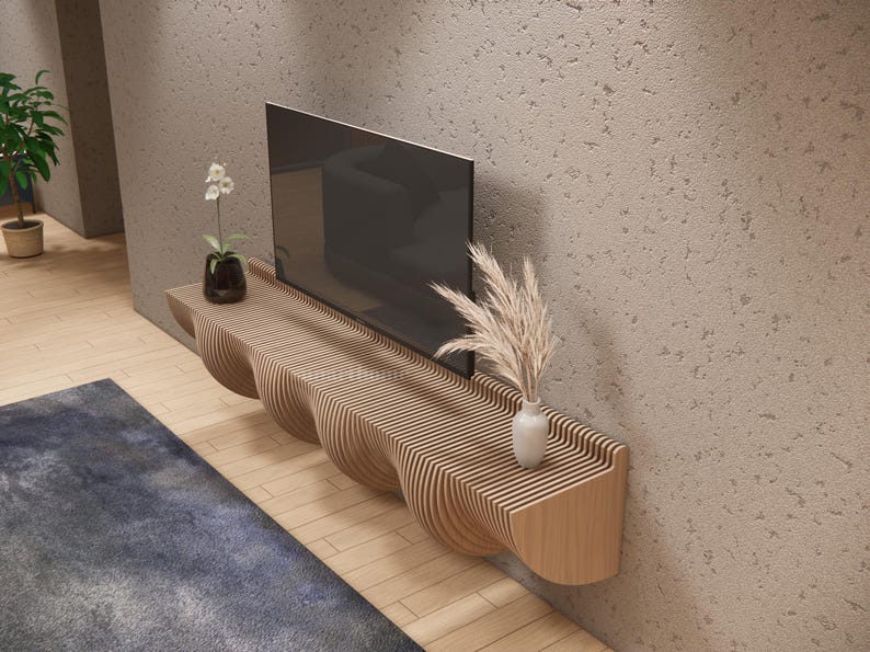 May include: A contemporary TV unit made of light-coloured wood, featuring a distinctive, undulating design. The unit is mounted on a textured wall and supports a large, black television. Decorative items include a vase with dried flowers and a small potted plant.