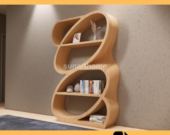 May include: A light-colored wooden bookshelf with a unique, flowing design. The shelves are filled with books, decorative items, and a small framed picture. The text "CNC FURNITURE FILE" and "CUTTING READY DXF FILE" are displayed.
