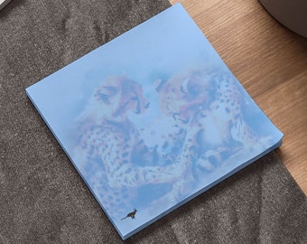 May include: A blue sticky note with a watercolor illustration of two cheetahs. The cheetahs are in a playful pose, with one cheetah's head resting on the other's back. The background is a light blue color.