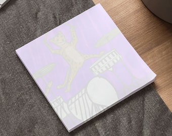 May include: A purple sticky note with a drawing of a cat playing the drums. The cat is yellow and has a white tail. The drums are white and have black stripes.