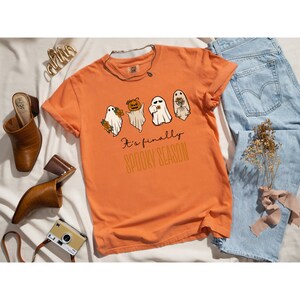 May include: Orange t-shirt with a graphic of four ghosts and the text "It's finally spooky season".
