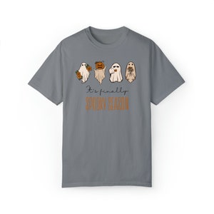 May include: A gray t-shirt with a graphic of four ghosts. The ghosts are wearing different accessories, including flowers, a pumpkin, and a camera. The text "It's finally spooky season" is printed below the ghosts.