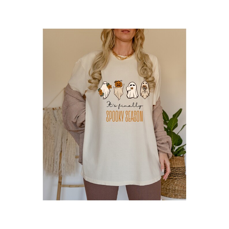May include: A white t-shirt with a graphic of four ghosts holding pumpkins and flowers. The text "It's finally spooky season" is printed below the ghosts.