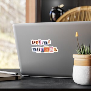 May include: A laptop computer with a sticker that says "Define normal" in colorful, cut-out letters.