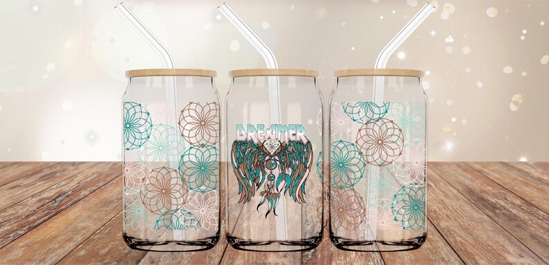 Peut inclure: Trois gobelets en verre en forme de canette avec des couvercles en bambou et des pailles en verre. Les gobelets sont d&eacute;cor&eacute;s de motifs de mandalas turquoise et bruns. Le gobelet du milieu porte le mot "DREAMER" en lettres turquoise et brunes avec un motif de capteur de r&ecirc;ves.