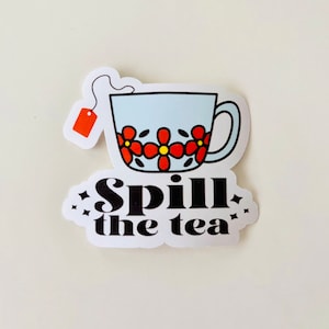 Puede incluir: Una taza de té blanca con un diseño floral rojo y amarillo y una bolsita de té colgando del borde. El texto "Spill the tea" está escrito debajo de la taza.