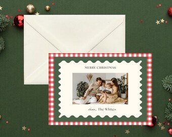 Może przedstawiać: Kartka świąteczna ze zdjęciem rodzinnym w zielono-czerwonej kratce vichy. Na kartce widnieje napis "Merry Christmas" i "love, The Whites" na kremowym tle. Za kartką leży koperta na ciemnozielonej powierzchni, z ozdobami świątecznymi.