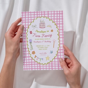 May include: A pink and white gingham patterned invitation card held by two hands. The card features an oval design with the text "Penelope is Two Fancy" and details for a second birthday party, including the date, time, and location.
