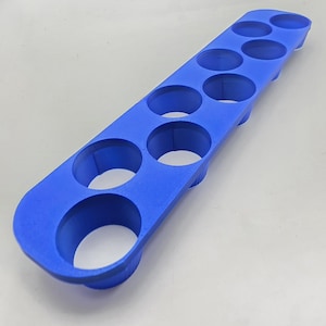 May include: A bright blue, rectangular object with multiple circular openings. The item appears to be a holder or organizer, possibly for small items or tools. The design is simple and functional, with a smooth, matte finish.