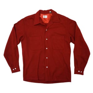Pode incluir: Uma camisa vermelha de botões de manga comprida com dois bolsos no peito. A camisa tem colarinho e é feita de um tecido macio e texturizado.
