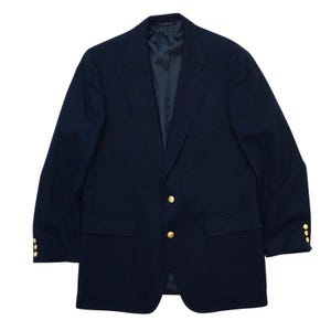 May include: A navy blue blazer with gold-colored buttons. The blazer has two front pockets and a notched lapel. The buttons are arranged in a double-breasted style. The jacket is made of a smooth fabric and appears to be a classic style.