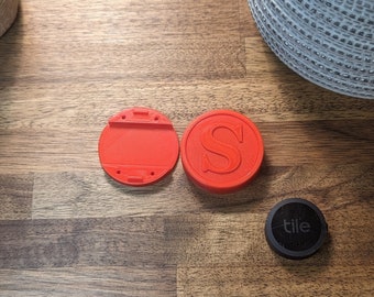 May include: Two red plastic tile trackers, one with the letter "S" on it, and one with a blank surface. A black Tile tracker with the word "tile" on it is also visible.