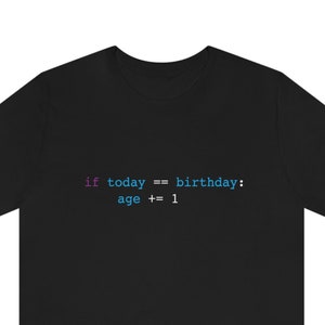 May include: Black t-shirt with the text "if today == birthday: age += 1" in a programming code style. The text is in shades of blue and purple. The shirt is made of a soft material.