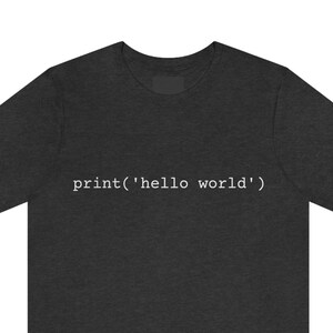 May include: Dark gray t-shirt with the text "print('hello world')" in white. The shirt is a crew neck style and appears to be made of a soft material. The text is centered on the front of the shirt.
