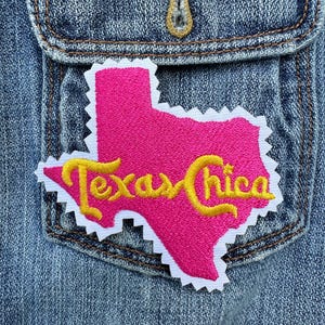 May include: A pink outline of the state of Texas with the words "Texas Chica" in yellow embroidery. The patch is on a blue denim background.