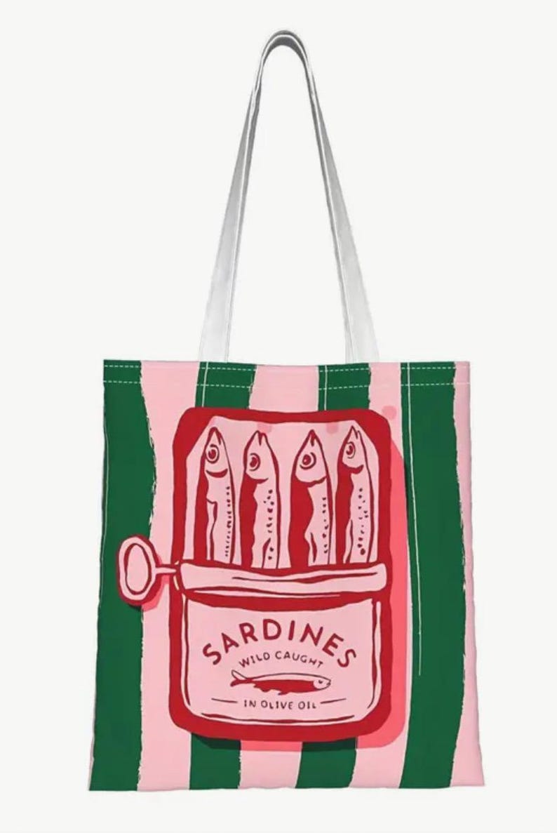May include: A tote bag with vertical pink and dark green stripes featuring a central graphic of an open red tin of sardines. The illustration shows four fish inside the tin with the text SARDINES WILD CAUGHT IN OLIVE OIL and a small fish icon.
