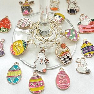 May include: A set of 14 gold-tone Easter-themed charms featuring bunnies, eggs, baskets, and the words "Happy Easter". The charms are attached to a clear glass wine glass charm holder.