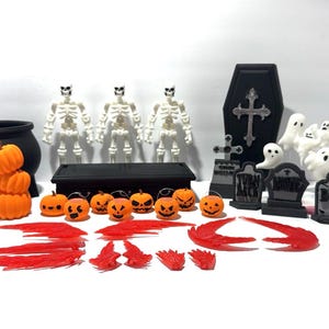 May include: A selection of Halloween decorations. Features orange pumpkins, skeleton figures, tombstones, ghosts, a cauldron, a coffin, and red flame-like accents. The items are arranged on a white surface.