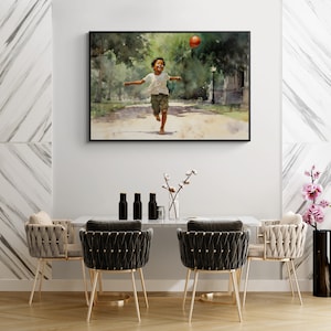 May include: A watercolor painting of a young boy running through a park with a red ball in the air. The painting is framed in a black frame and is hanging on a white wall.