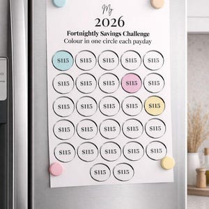 May include: A white paper savings challenge chart for 2026, held on a refrigerator with colorful magnets. The chart has circles with the amount $115, designed to be colored in each payday. The text reads "Fortnightly Savings Challenge".