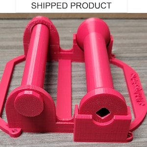 May include: A vibrant red 3D-printed item, comprising two cylindrical parts with rounded ends, linked by a central support. It has a handle and a square aperture. The text "SHIPPED PRODUCT" is displayed at the top of the image.